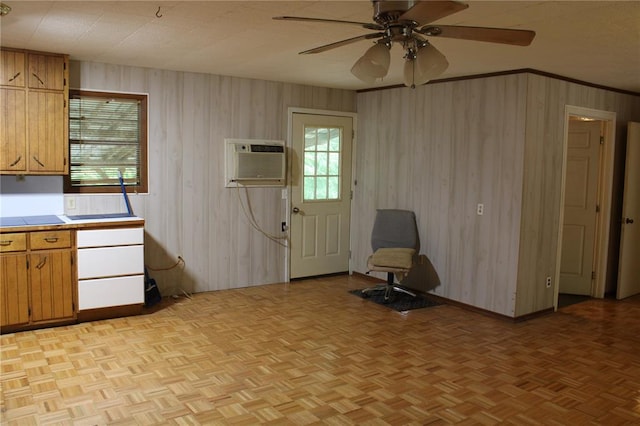 kitchen with a wall mounted air conditioner, tile counters, ceiling fan, brown cabinetry, and wood walls
