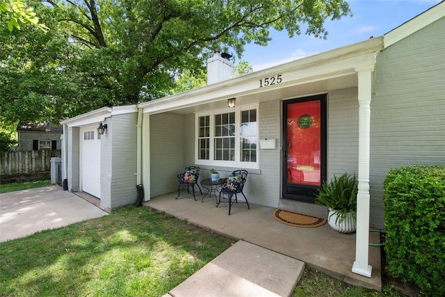 doorway to property featuring brick siding, a chimney, a porch, concrete driveway, and fence