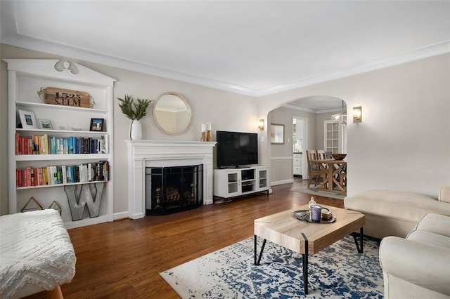 living area featuring arched walkways, wood finished floors, crown molding, and a fireplace