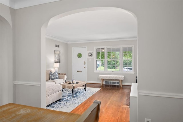 living room featuring arched walkways, wood finished floors, ornamental molding, and baseboards