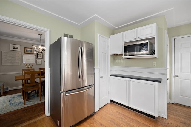 kitchen with appliances with stainless steel finishes, white cabinets, light wood-style floors, and a chandelier