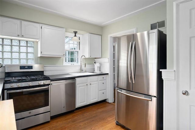kitchen featuring stainless steel appliances, a sink, white cabinets, and wood finished floors