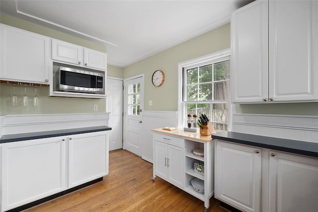kitchen with stainless steel microwave, white cabinetry, light wood-style floors, and wainscoting