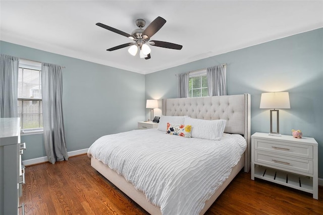 bedroom featuring multiple windows, dark wood finished floors, baseboards, and ceiling fan