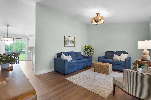living area with dark wood-style floors, baseboards, a chandelier, and vaulted ceiling