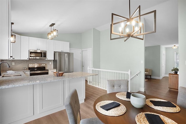 kitchen featuring appliances with stainless steel finishes, a sink, light wood-style floors, backsplash, and a peninsula