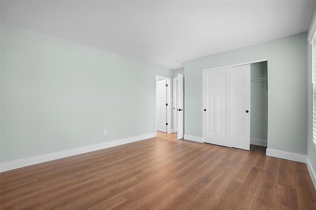 unfurnished bedroom featuring wood finished floors, baseboards, and a closet