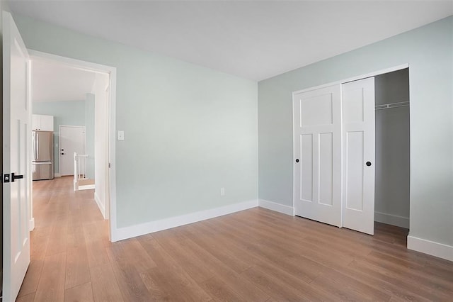 unfurnished bedroom with freestanding refrigerator, light wood-style floors, and baseboards