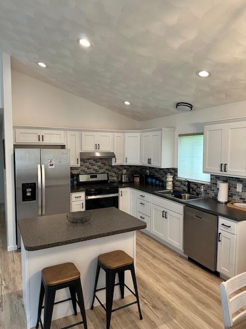 kitchen with appliances with stainless steel finishes, lofted ceiling, dark countertops, white cabinets, and tasteful backsplash