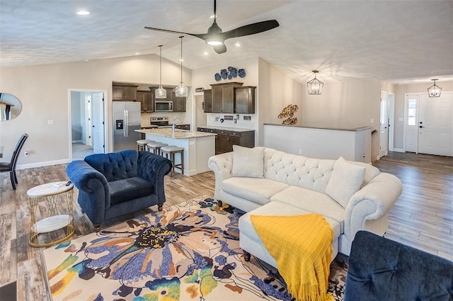 living area with lofted ceiling, light wood-style flooring, baseboards, and a ceiling fan