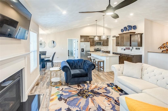living area featuring vaulted ceiling, light wood-style flooring, ceiling fan, baseboards, and a fireplace