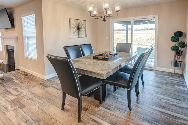 dining room featuring a chandelier, baseboards, hardwood / wood-style flooring, and a glass covered fireplace