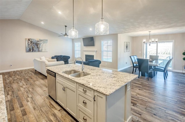 kitchen with a sink, stainless steel dishwasher, open floor plan, wood finished floors, and baseboards