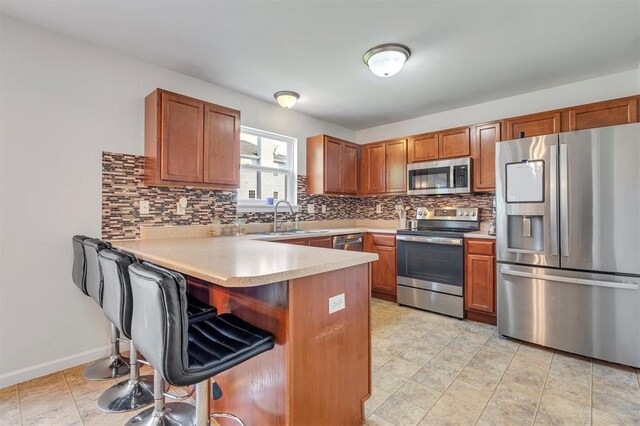kitchen with stainless steel appliances, a sink, a peninsula, backsplash, and light countertops
