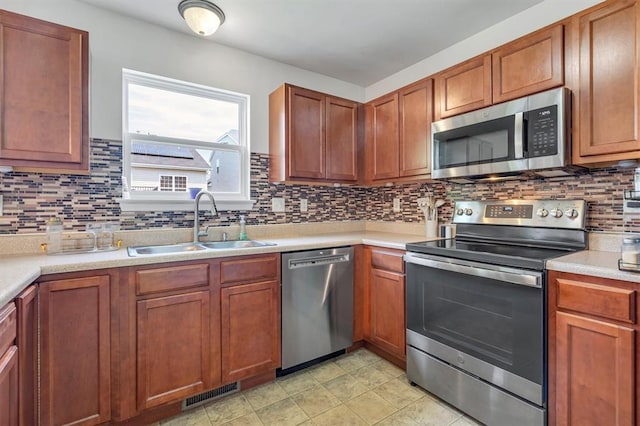 kitchen featuring stainless steel appliances, a sink, backsplash, light countertops, and brown cabinets