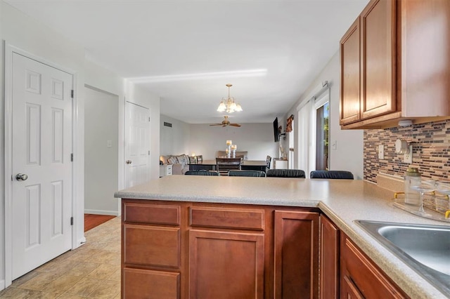 kitchen featuring a peninsula, a chandelier, tasteful backsplash, a sink, and light countertops