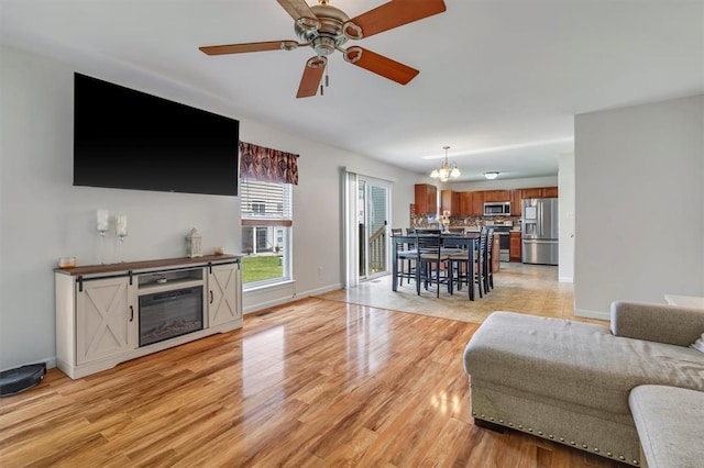 living room featuring a chandelier, light wood-style flooring, baseboards, and ceiling fan