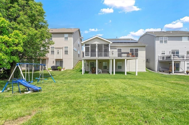 rear view of house featuring a sunroom, a yard, a deck, and a playground