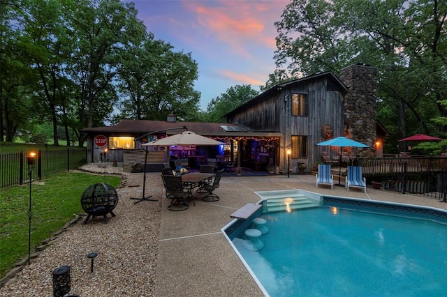 pool at dusk featuring a fire pit and a patio