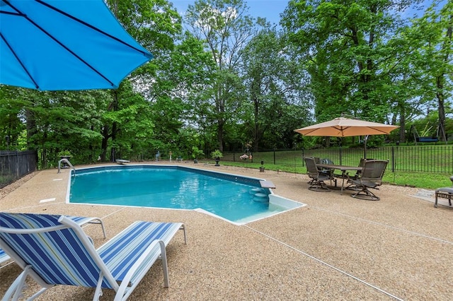 view of pool with a patio area and view of wooded area