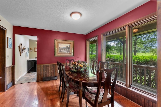 dining space featuring a textured ceiling, wood-type flooring, and wainscoting