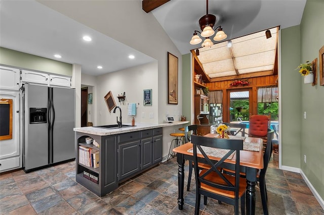 kitchen with stainless steel fridge with ice dispenser, a sink, stone tile flooring, white cabinetry, and a peninsula