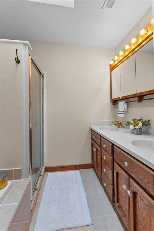 bathroom with a stall shower, tile patterned floors, double vanity, and baseboards