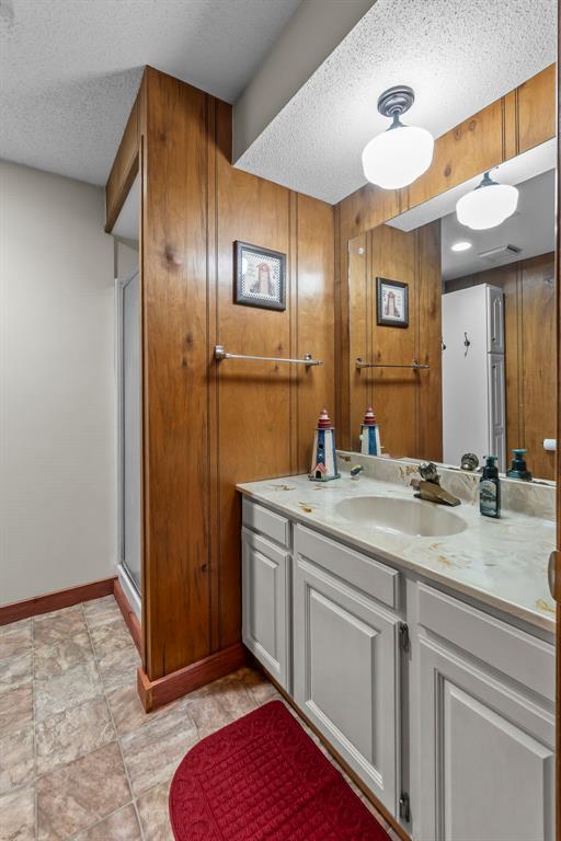 full bath with a textured ceiling, vanity, baseboards, and a shower with door