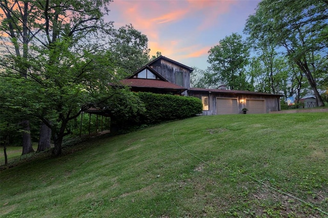 yard at dusk with a lawn, a garage, and driveway