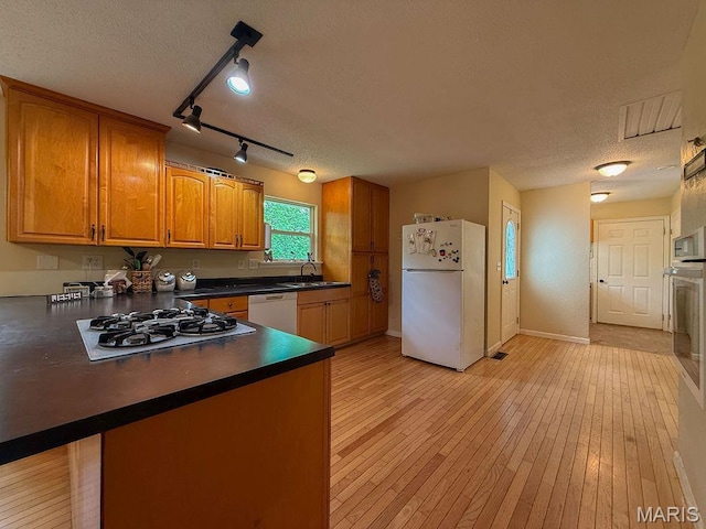 524 Arrowhead Pt, Cedar Hill, MO 63016 - kitchen featuring white appliances, a textured ceiling, dark countertops, a peninsula, and brown cabinetry