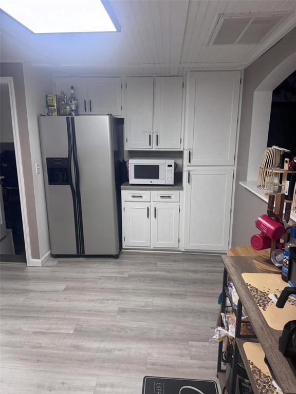 313 W Crumb Ave, Bernie, MO 63822 - kitchen with stainless steel fridge, white microwave, white cabinets, arched walkways, and light wood-style flooring