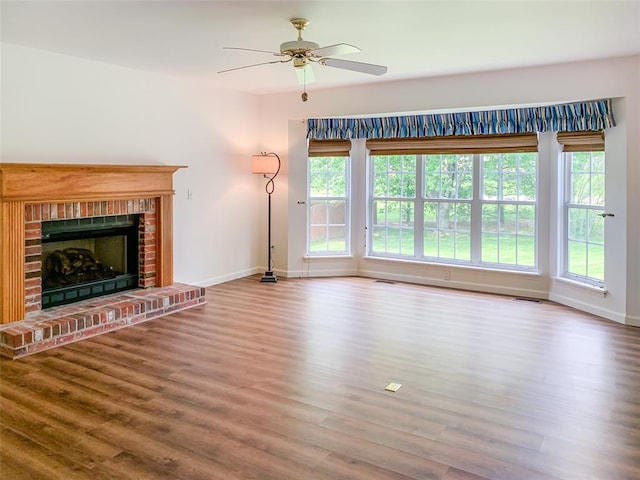 unfurnished living room featuring baseboards, wood finished floors, a ceiling fan, and a brick fireplace