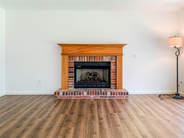 unfurnished living room with baseboards, wood finished floors, and a brick fireplace