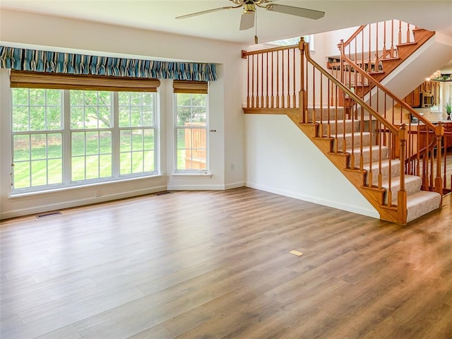 unfurnished living room featuring a ceiling fan, wood finished floors, baseboards, and stairs