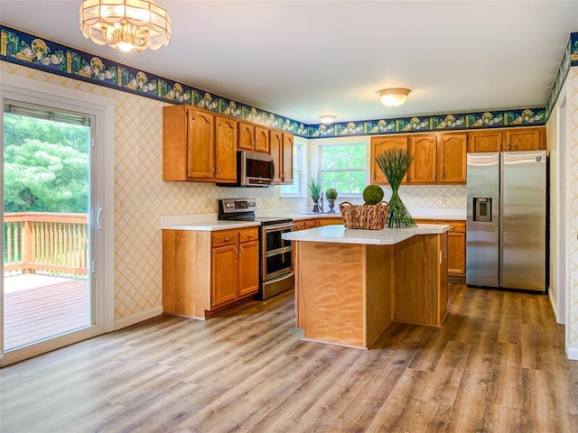kitchen with appliances with stainless steel finishes, wallpapered walls, light countertops, brown cabinets, and wood finished floors
