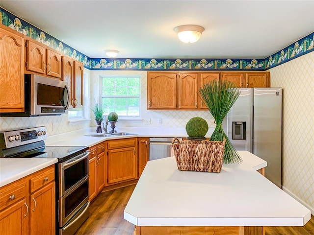 kitchen featuring stainless steel appliances, wallpapered walls, dark wood-style floors, light countertops, and a sink
