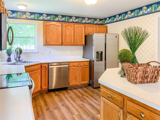 kitchen featuring wallpapered walls, appliances with stainless steel finishes, a sink, light countertops, and light wood finished floors