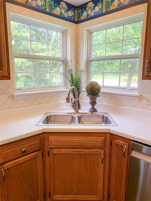 kitchen featuring stainless steel dishwasher, a sink, light countertops, and brown cabinetry
