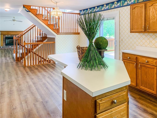 kitchen featuring wallpapered walls, light countertops, ceiling fan, brown cabinetry, and wood finished floors