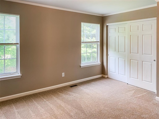 unfurnished bedroom with multiple windows, carpet flooring, baseboards, a closet, and ornamental molding