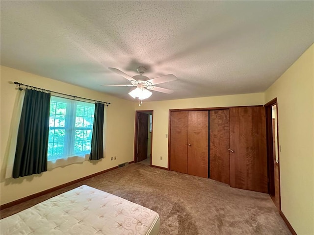 unfurnished bedroom featuring carpet floors, a textured ceiling, a closet, ceiling fan, and baseboards
