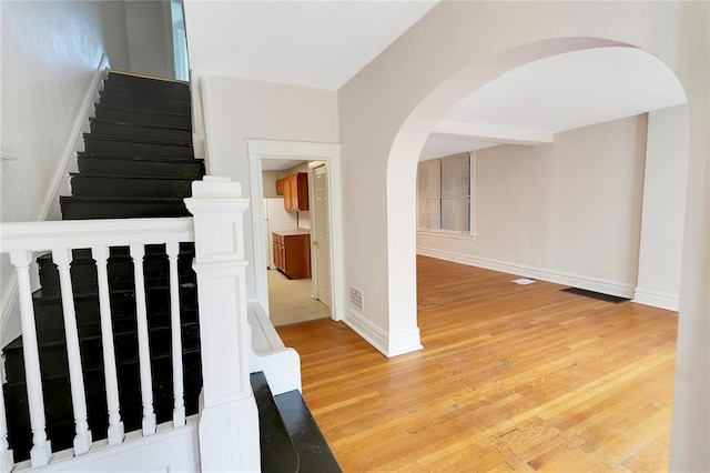 stairs featuring arched walkways, wood finished floors, and baseboards