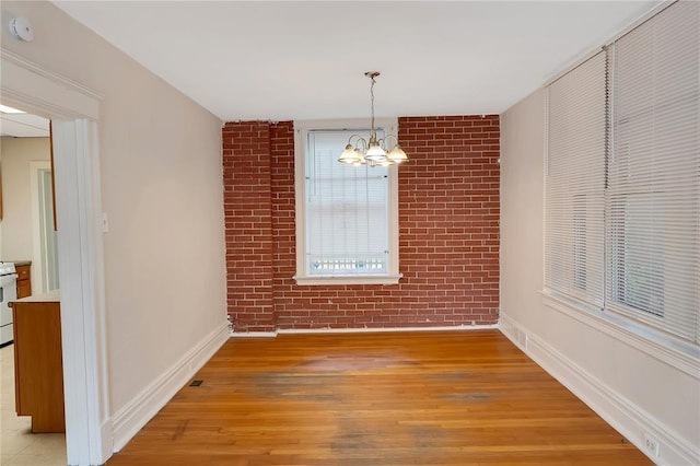 unfurnished dining area with a chandelier, brick wall, light wood-style flooring, and baseboards