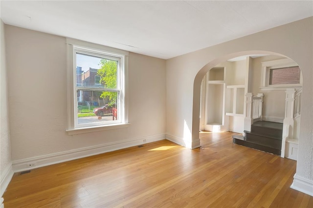 unfurnished room with arched walkways, light wood finished floors, stairway, and baseboards