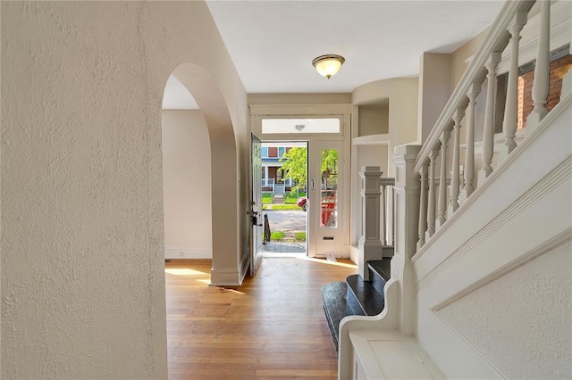foyer entrance featuring a textured wall, wood finished floors, arched walkways, stairs, and baseboards