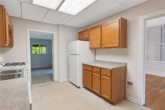 kitchen featuring a sink, freestanding refrigerator, a drop ceiling, light countertops, and baseboards