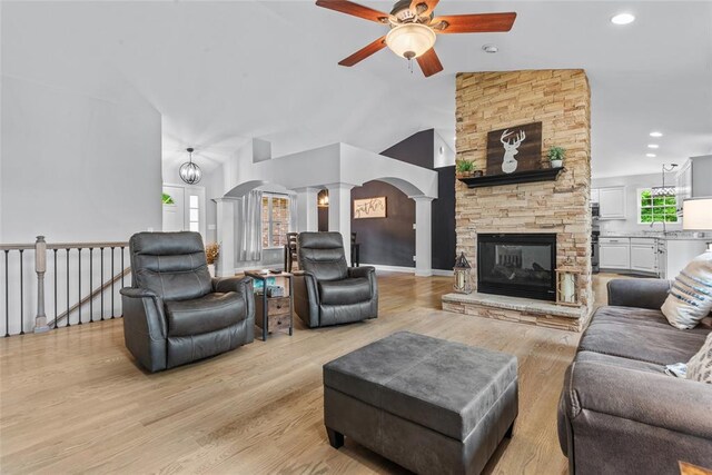 living area with a ceiling fan, arched walkways, light wood-style floors, ornate columns, and a fireplace
