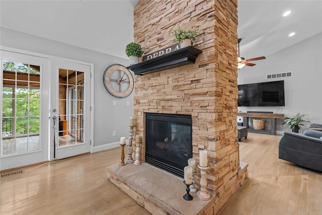 living room with wood finished floors, a stone fireplace, a ceiling fan, baseboards, and high vaulted ceiling
