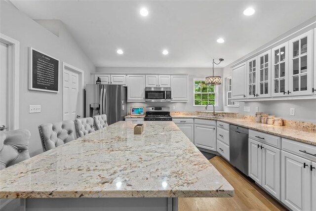 kitchen with stainless steel appliances, a sink, a center island, light wood-type flooring, and light stone countertops