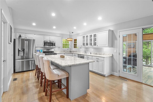 kitchen with stainless steel appliances, a center island, white cabinetry, recessed lighting, and light stone counters